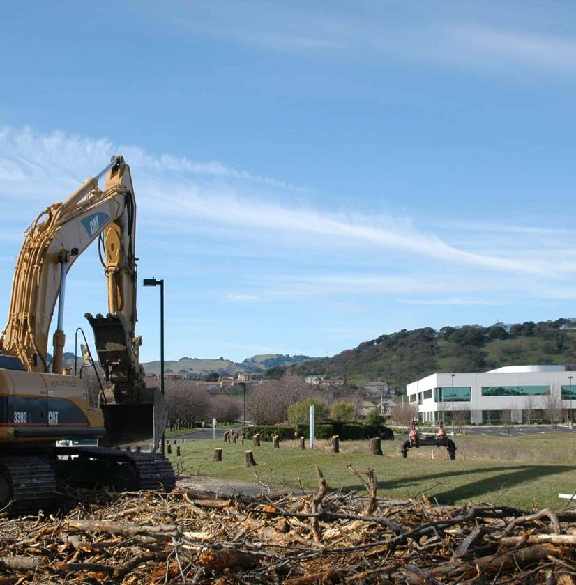 CAT excavator clearing debris pile with mountains and buildings behind