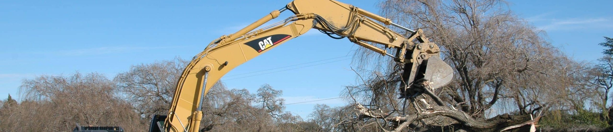 CAT excavator with grapple attachment clearing large pile of tree debris