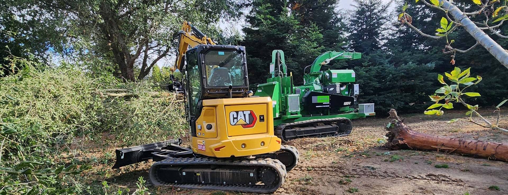 Yellow CAT excavator and green wood chipper on tree removal job site